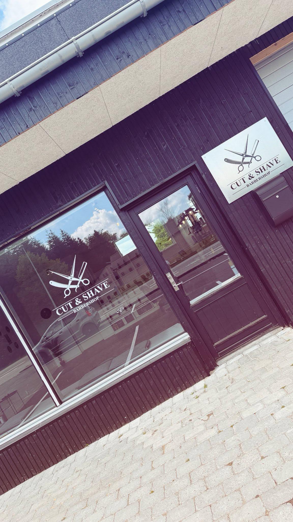 Frisørsalon med store vinduer og skilt med saks, beliggende i en sort bygning.