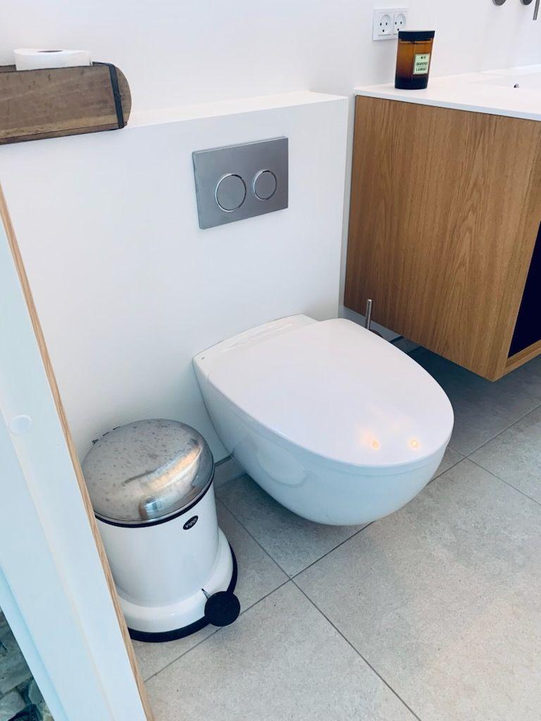 Moderne badeværelse med væghængt toilet og affaldsspand i rustfrit stål ved siden af.