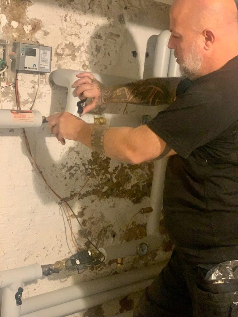 En mand arbejder med rørinstallation i en kælder, mens han justerer ventiler og ledninger.