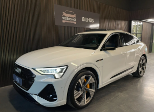 En hvid Audi E-Tron GT parkeret i et moderne bilhus med en mørk baggrund.