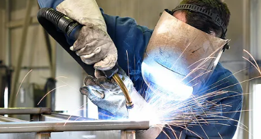 En svejser arbejder med en svejsemaskine, der producerer gnister i en fabrik.