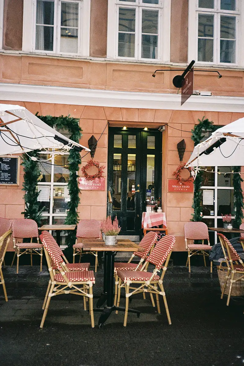 En terrasse med flere stole og parasoller, med udsigt til gaden og bygninger i baggrunden, der skaber en hyggelig udendørs spiseatmosfære.